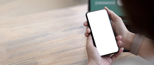 Imagen de maqueta en blanco teléfono celular con pantalla blanca. Mano de mujer sosteniendo mensajes de texto usando el móvil en el escritorio en la oficina en casa.