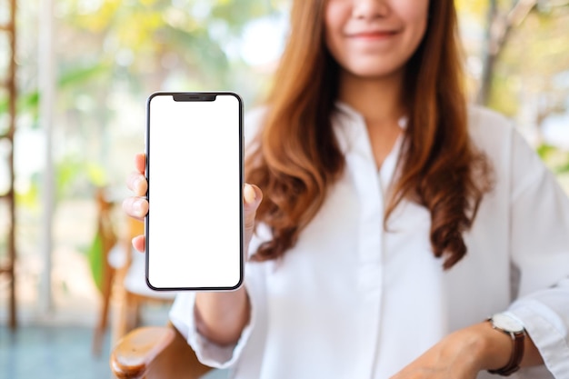 Imagen de maqueta de una hermosa mujer sosteniendo y mostrando un teléfono móvil con pantalla en blanco en la cafetería