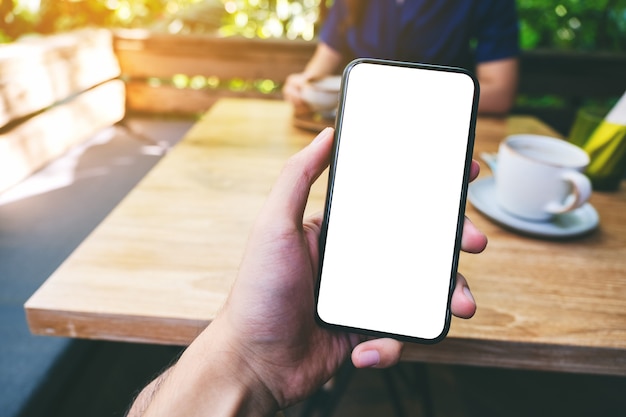 Foto imagen de maqueta de un hombre que sostiene un teléfono móvil negro con pantalla en blanco con una mujer tomando café en la cafetería