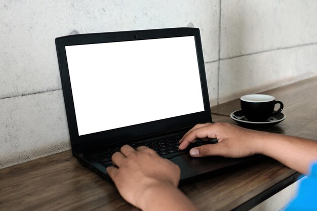 Imagen de una maqueta de un hombre que usa y trabaja en una computadora portátil con una pantalla blanca en blanco con una taza de café en una mesa de madera