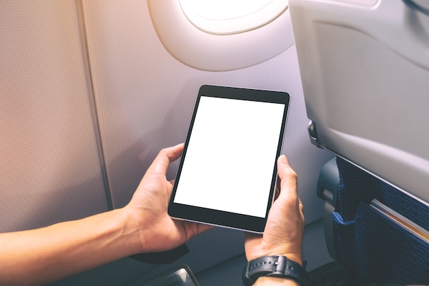 Imagen de maqueta de un hombre sosteniendo y mirando un tablet pc negro con una pantalla de escritorio en blanco junto a la ventana de un avión