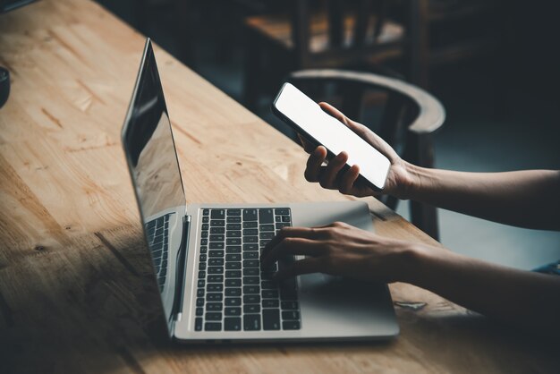 Imagen de la maqueta de la mano de una mujer trabajando en una computadora portátil y un teléfono inteligente con pantalla de espacio de copia de escritorio en blanco en un escritorio