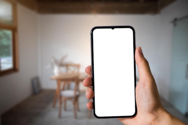 Imagen de la maqueta de la mano que sostiene el teléfono móvil blanco con pantalla en blanco en la cafetería.