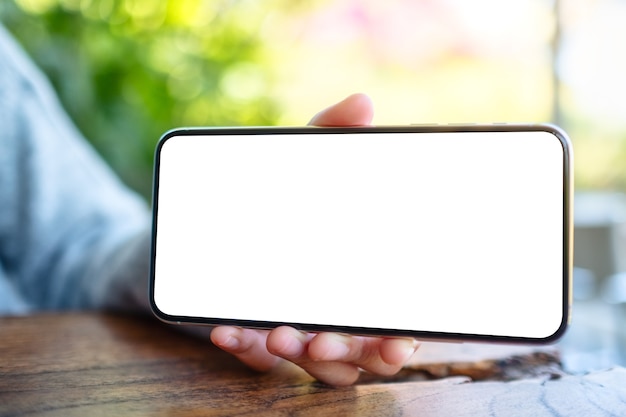 Foto imagen de maqueta de una mano sosteniendo y mostrando un teléfono móvil negro con pantalla de escritorio en blanco