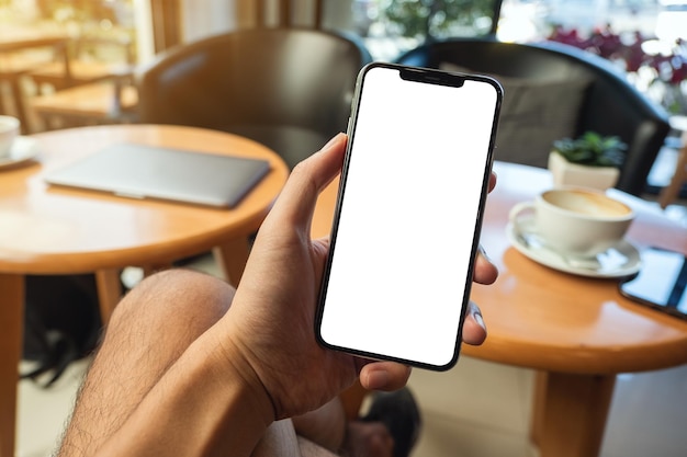 Foto imagen de maqueta de una mano sosteniendo y mostrando un teléfono móvil con pantalla blanca en blanco en la cafetería