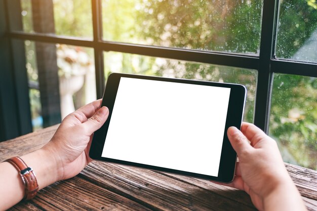 Imagen de maqueta de manos sosteniendo tablet pc negro con pantalla de escritorio blanca en blanco