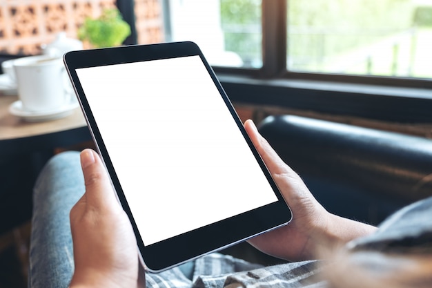 Imagen de maqueta de manos sosteniendo tablet pc negro con pantalla de escritorio blanco en blanco mientras está sentado en la cafetería