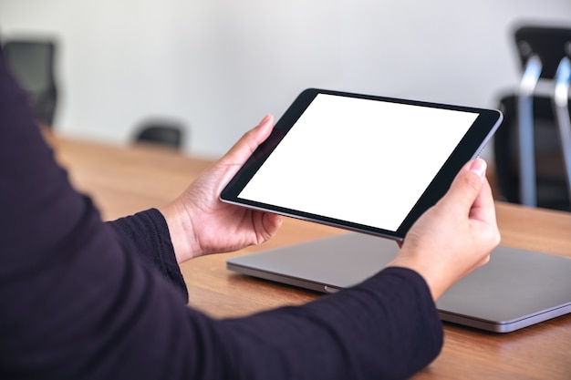 Imagen de maqueta de manos sosteniendo y usando una tableta negra con pantalla de escritorio en blanco