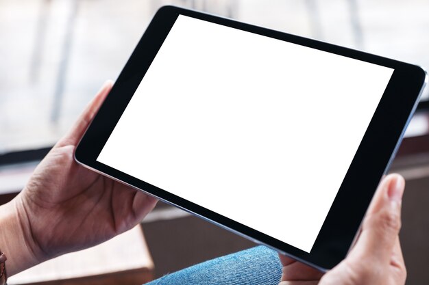 Imagen de maqueta de una mujer que sostiene un tablet pc negro con pantalla en blanco mientras está sentado en la cafetería