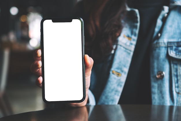 Imagen de maqueta de una mujer sosteniendo y mostrando un teléfono móvil negro con pantalla en blanco en el café