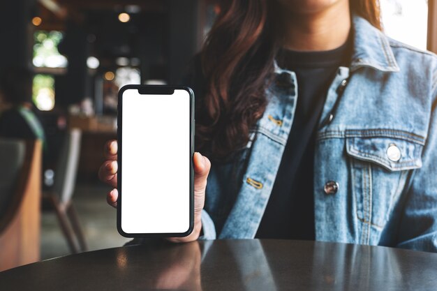 Imagen de maqueta de una mujer sosteniendo y mostrando un teléfono móvil negro con pantalla en blanco en el café