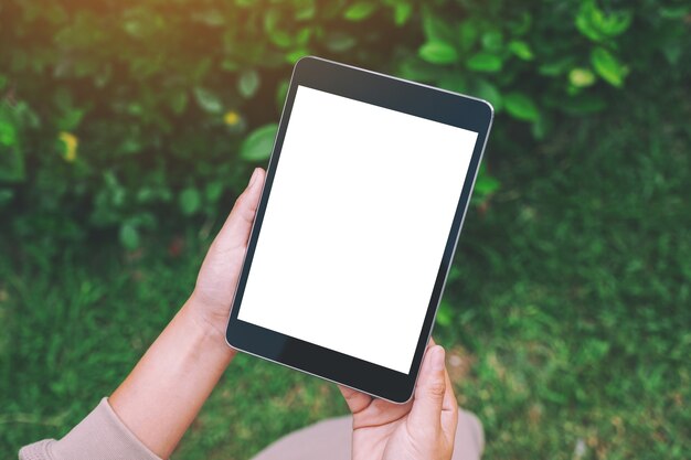 Imagen de maqueta de una mujer sosteniendo una tablet pc negra con una pantalla de escritorio en blanco en el parque