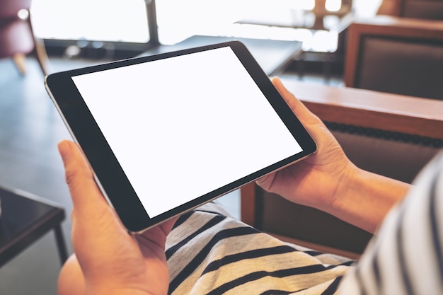 Imagen de maqueta de una mujer sosteniendo tablet pc negro con pantalla en blanco horizontalmente mientras está sentado en la cafetería