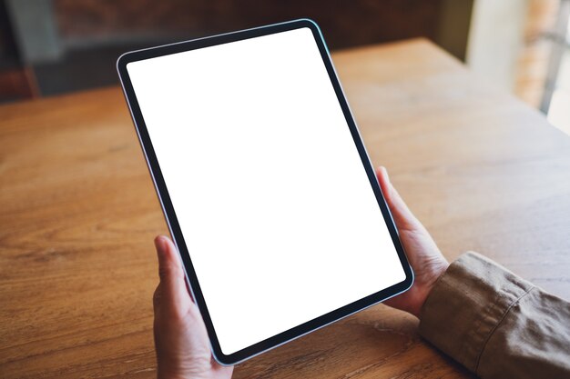 Imagen de maqueta de una mujer sosteniendo tablet pc negro con pantalla en blanco en la mesa de madera