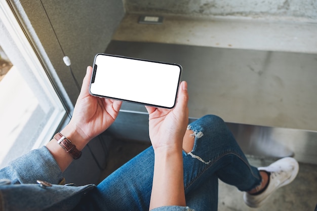 Imagen de maqueta de una mujer sosteniendo un teléfono móvil negro con pantalla en blanco