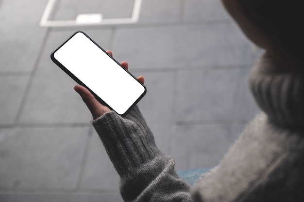 Imagen de maqueta de una mujer sosteniendo un teléfono móvil negro con una pantalla de escritorio en blanco al aire libre