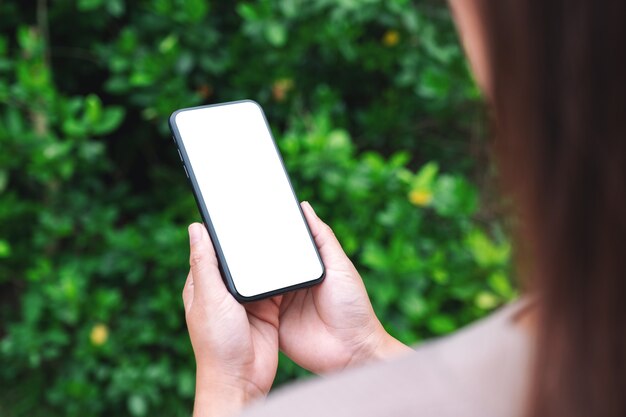 Imagen de maqueta de una mujer sosteniendo un teléfono móvil negro con pantalla de escritorio en blanco con fondo de naturaleza verde