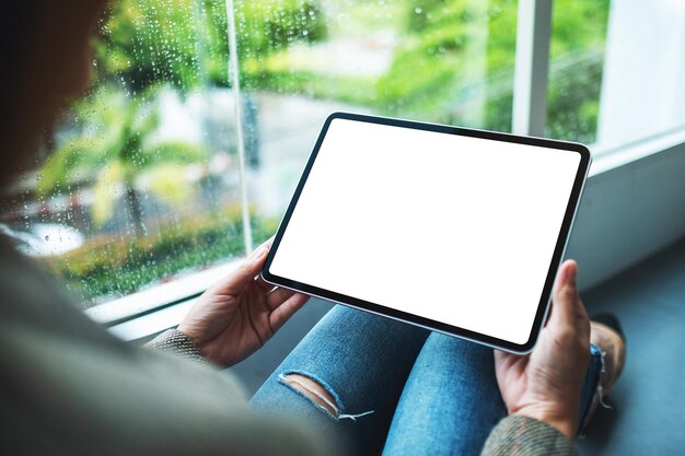 Imagen de maqueta de una mujer sosteniendo y usando una tableta digital con una pantalla de escritorio blanca en blanco mientras está sentada en el piso