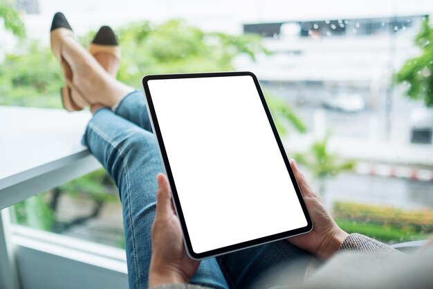 Imagen de maqueta de una mujer sosteniendo y usando una tableta digital con una pantalla de escritorio en blanco mientras está sentada en la oficina