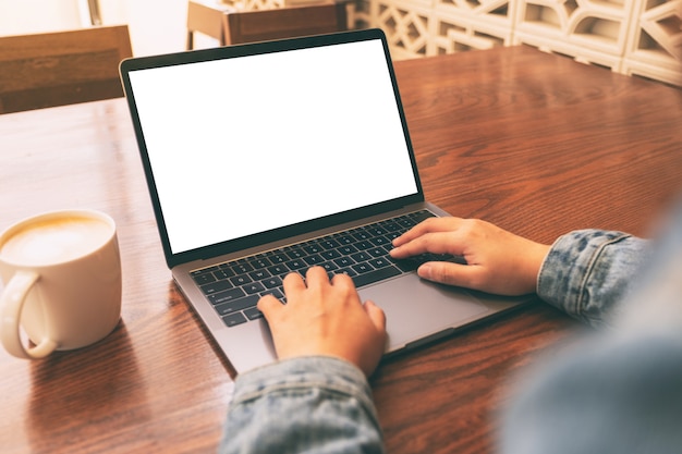 Imagen de maqueta de una mujer usando y escribiendo en una computadora portátil con pantalla en blanco y una taza de café en la mesa de madera