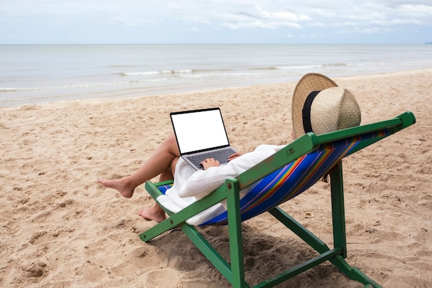 Imagen de maqueta de una mujer usando y escribiendo en una computadora portátil con pantalla de escritorio en blanco mientras está acostada en una silla de playa