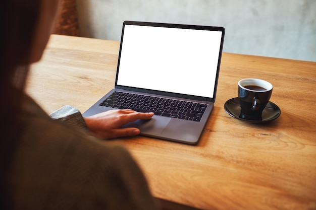 Imagen de maqueta de una mujer usando y tocando en el panel táctil de la computadora portátil con pantalla de escritorio en blanco con una taza de café en la mesa de madera