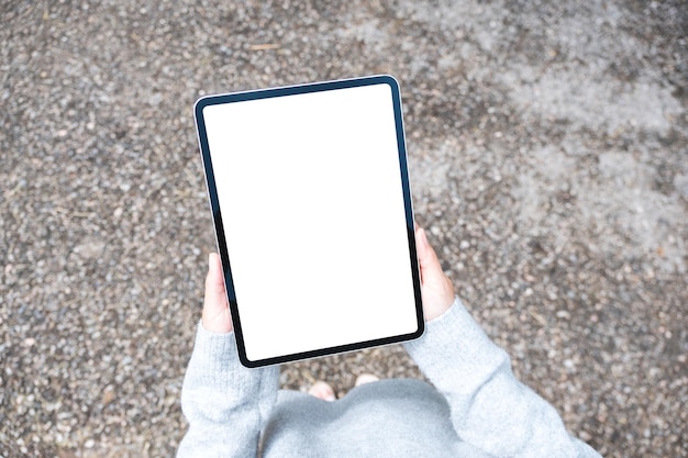 Imagen de maqueta de vista superior de una mujer que sostiene una tableta digital con una pantalla de escritorio blanca en blanco al aire libre