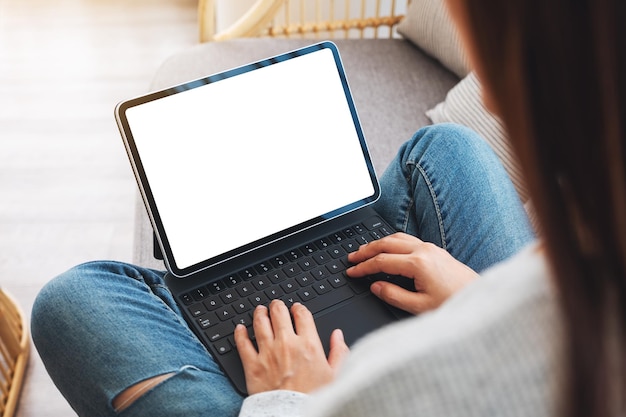 Imagen de la maqueta de la vista superior de una mujer que usa y escribe en un tablet pc negro con una pantalla blanca de escritorio en blanco como un pc mientras está sentado en un sofá en casa