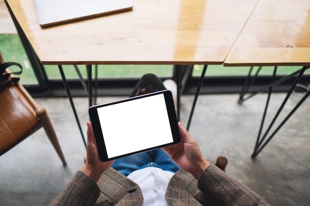 Imagen de la maqueta de la vista superior de una mujer sentada y sosteniendo una tablet pc negra con una pantalla de escritorio en blanco en blanco