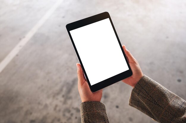 Imagen de maqueta de vista superior de una mujer sosteniendo tablet pc negro con pantalla en blanco en la calle