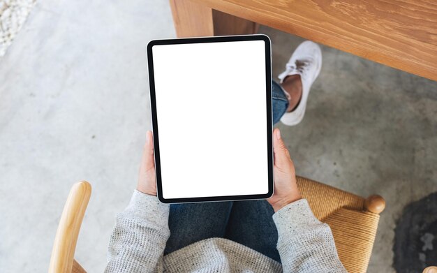 Imagen de maqueta de vista superior de una mujer sosteniendo tablet pc negro con pantalla de escritorio en blanco en blanco