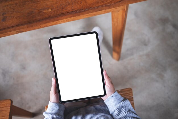 Imagen de maqueta de vista superior de una mujer sosteniendo tableta digital con pantalla de escritorio en blanco en blanco