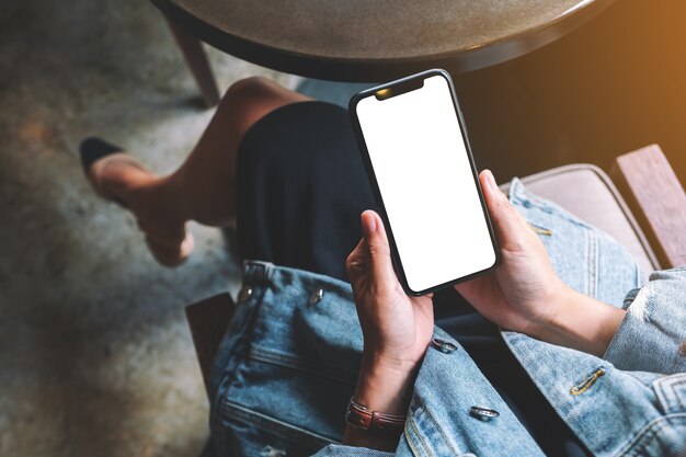 Imagen de maqueta de vista superior de una mujer sosteniendo un teléfono móvil negro con pantalla en blanco en café