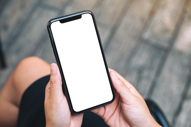 Foto imagen de maqueta de vista superior de una mujer sosteniendo un teléfono móvil negro con pantalla de escritorio blanca en blanco