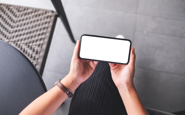 Imagen de maqueta de vista superior de una mujer sosteniendo un teléfono móvil con pantalla de escritorio en blanco en blanco