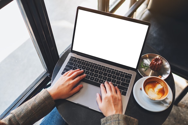 Imagen de maqueta de vista superior de una mujer usando y escribiendo en una computadora portátil con pantalla de escritorio blanca en blanco en café