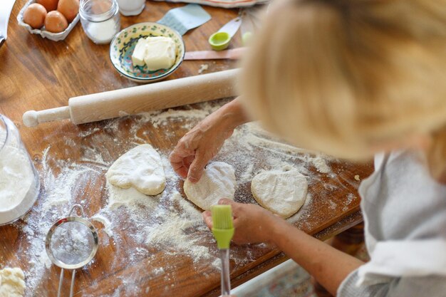 Imagen de marco de manos femeninas sosteniendo la masa en la vista superior en forma de corazón. Ingredientes para hornear en la mesa de madera oscura. Vista horizontal.