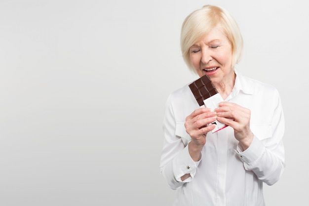 Una imagen de mautre lady eading una barra de chocolate con leche. A ella le gusta comer dulces. Ella se preocupa mucho por su salud, pero por el momento quiere disfrutar el sabor del chocolate.