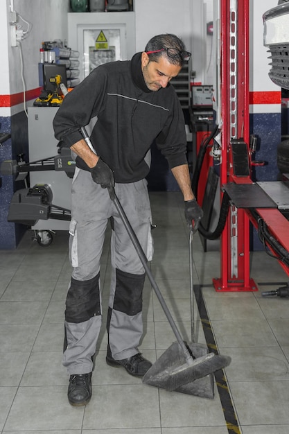 Imagen de un mecánico barriendo el suelo de su taller con una escoba