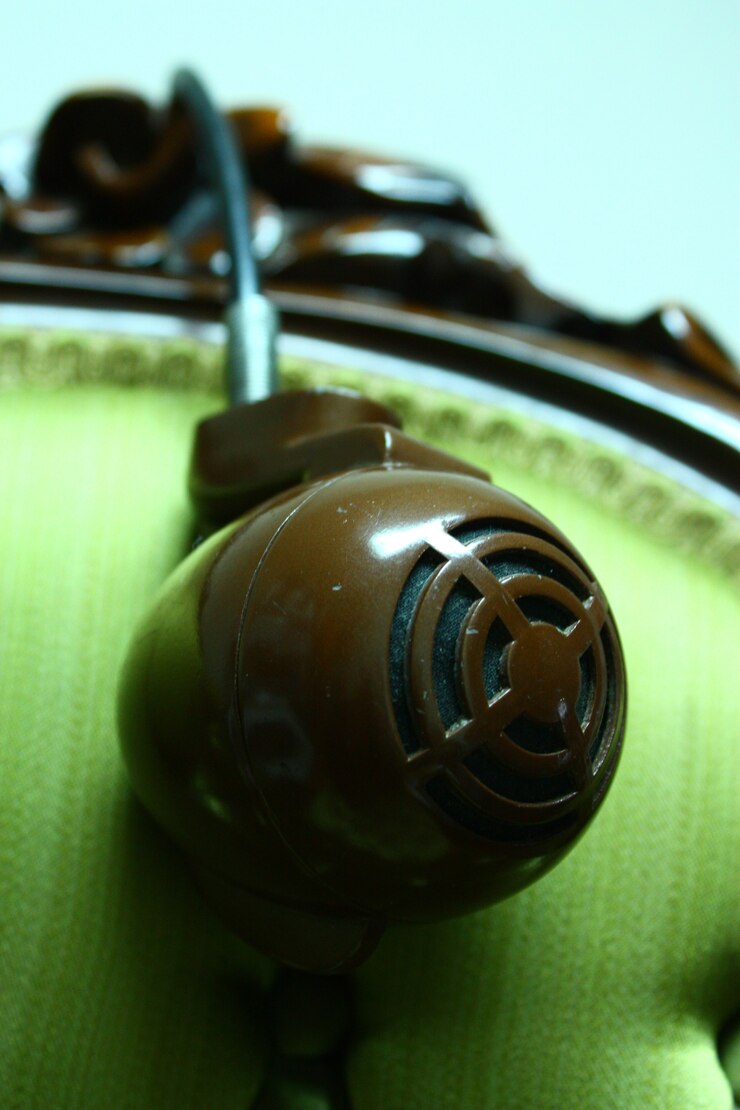 Foto imagen de un micrófono circular antiguo cuelga de un cordón negro sobre el respaldo de una silla con tapizado de color amarillo verdoso