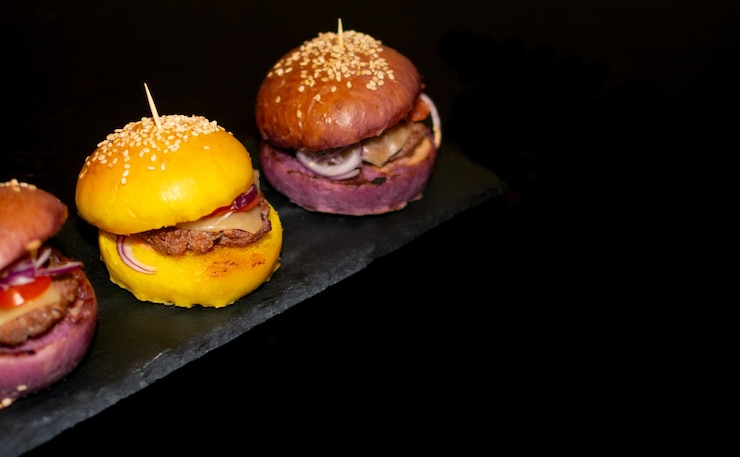Imagen de mini hamburguesas gourmet de colores con semillas de sésamo sobre pizarra negra