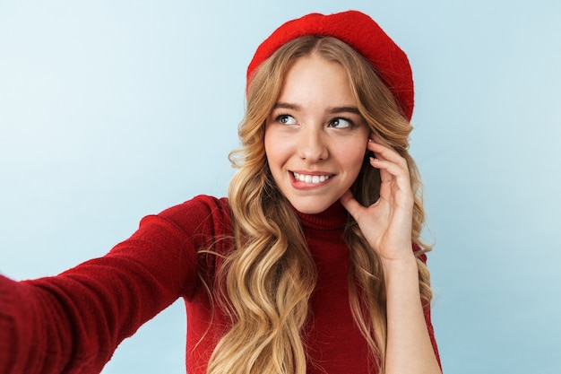 Imagen de moda mujer rubia de 20 años vistiendo boina roja sonriendo mientras toma selfie foto, aislado