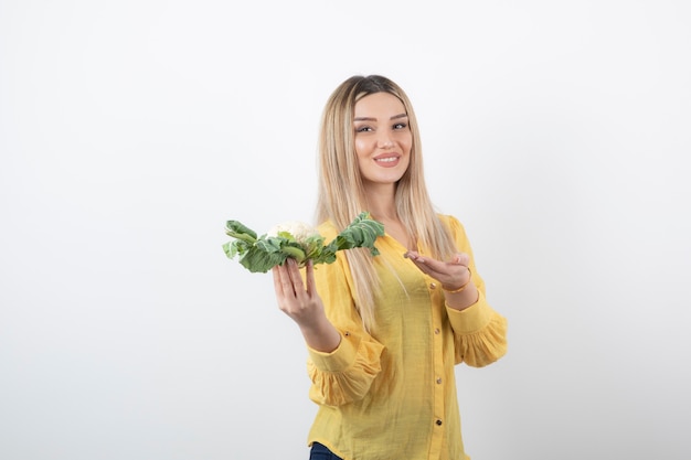 Imagen de un modelo de mujer bonita sonriente de pie y sosteniendo coliflor.