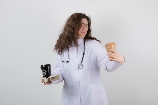 Imagen de una modelo de mujer joven en uniforme blanco sosteniendo un cartón con tazas de café.