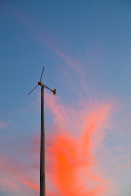 Imagen del molino de viento en un cielo mayormente azul con nubes de neón naranja