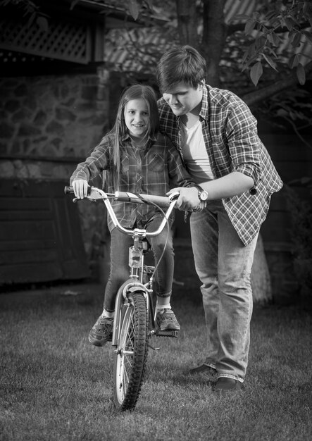 Imagen monocroma de padre feliz enseñando a su hija a andar en bicicleta