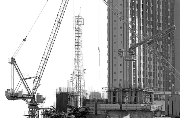 Imagen monocromática de grúas trabajando en el sitio de construcción con una torre de telecomunicaciones en el fondo