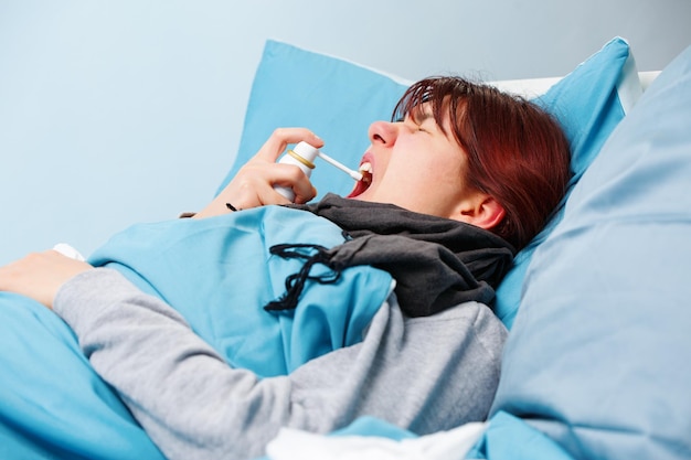 Imagen de una morena enferma usando spray para la garganta acostada en la cama