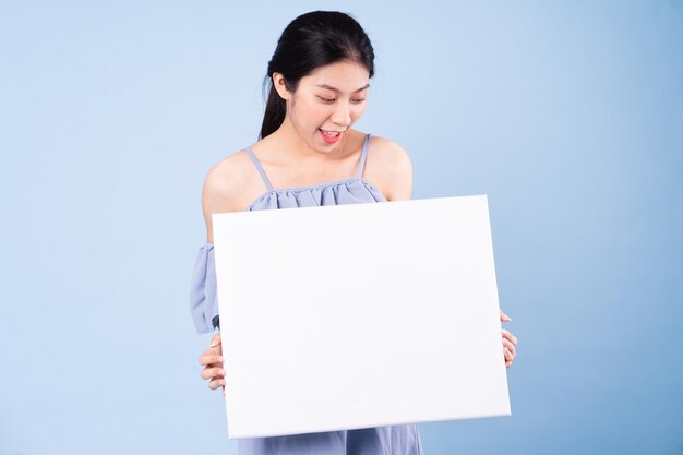 Imagen de la muchacha asiática que sostiene el tablero blanco, aislado en fondo azul