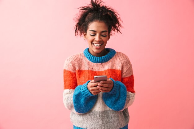 Imagen de una mujer africana joven hermosa feliz posando aislada mediante teléfono móvil.